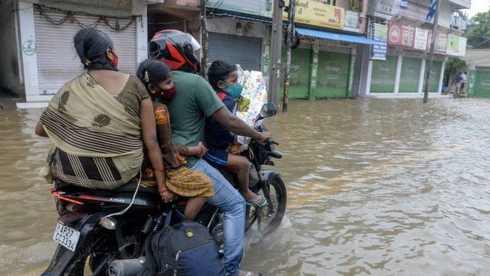 Motorists riding a scooter make their way on a flooded street following heavy rains in Hyderabad on October 14, 2020.