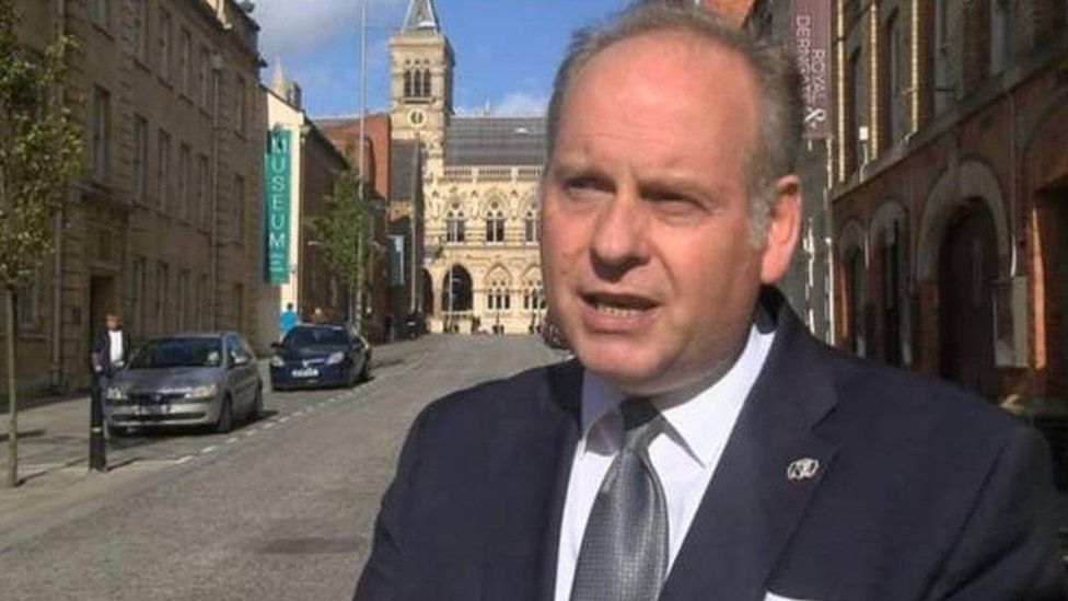 Man wit short hair wearing a suit and tie stands with Northampton Guildhall in the background