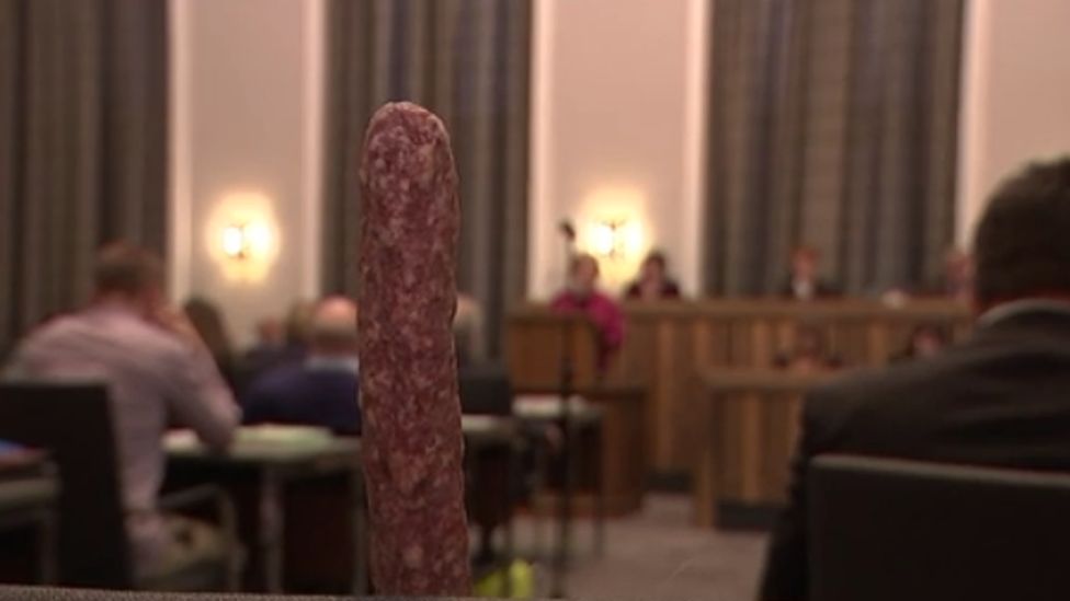 A still from the news report, where the ahle wurst sausage is on a chair at the council meeting