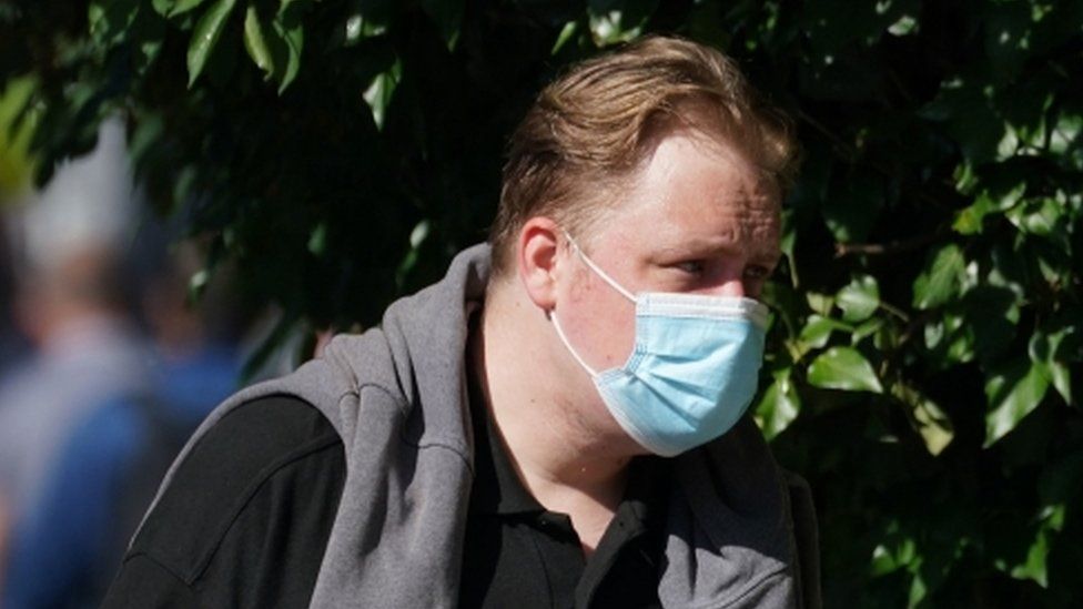 A head and shoulders shot of Darren Hurrell wearing a facemask with a sweater over his shoulders