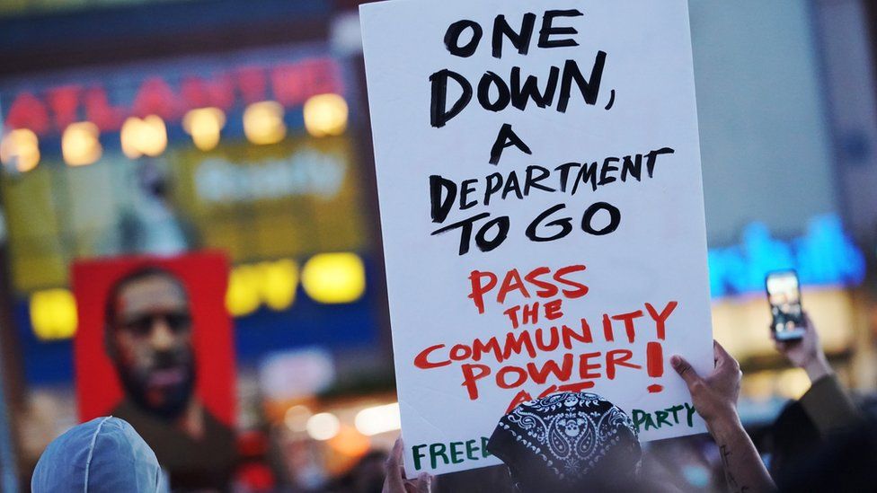 A man holds up a sign saying "one down, a department to go"