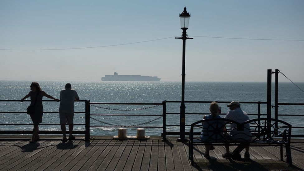 People on a pier overlooking the sea with a ship in the hazy distance