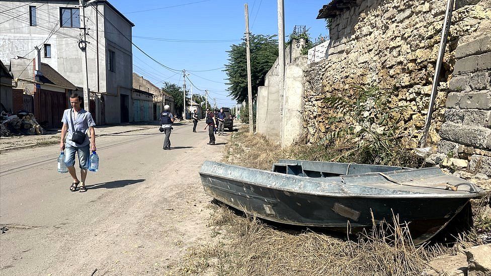 Небольшая лодка стоит на обочине дороги в Херсоне, Украина, пока жители несут воду в бутылках