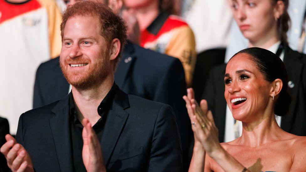 Prince Harry standing next to Meghan during a closing ceremony of the Invictus Games in 2023. They are both smiling and clapping
