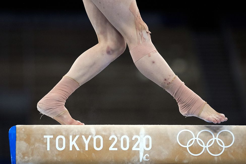 Гуань Ченчен выигрывает золотую медаль, выступая на бревне с синяками, покрывающими ноги, в Токио, Япония, 3 августа 2021 года,