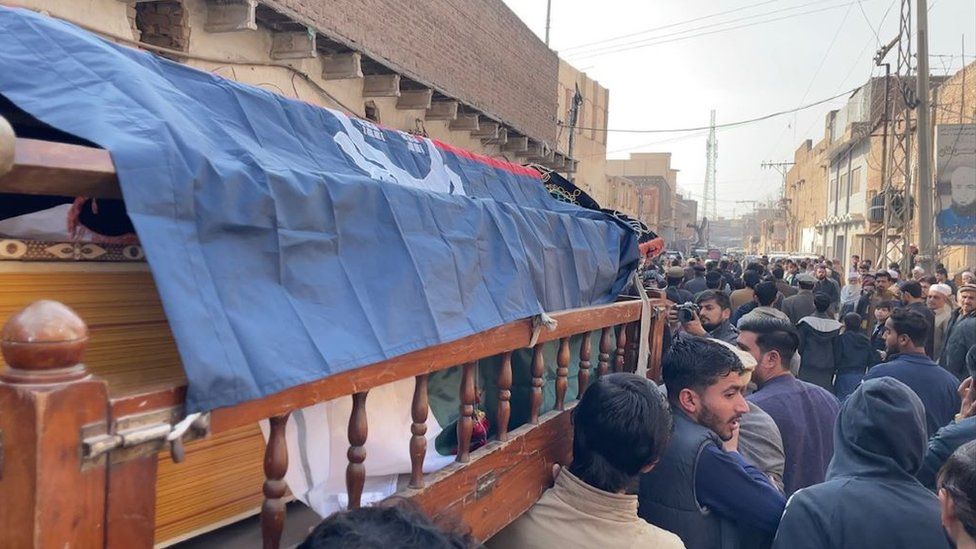 Close of Irfan Ullah's coffin being carried through street, surrounded by men