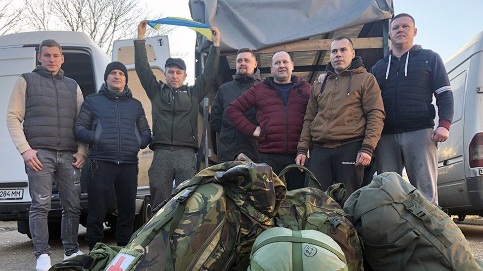 Ukrainian men from London stand in front of a van full of surplus army gear