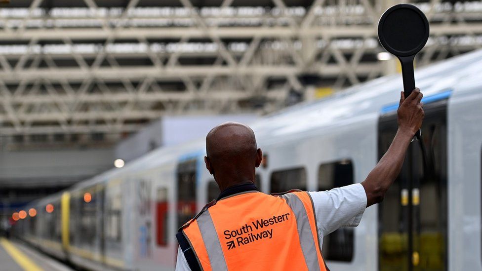 A member of rail staff holds up a dispatch baton at Waterloo Station