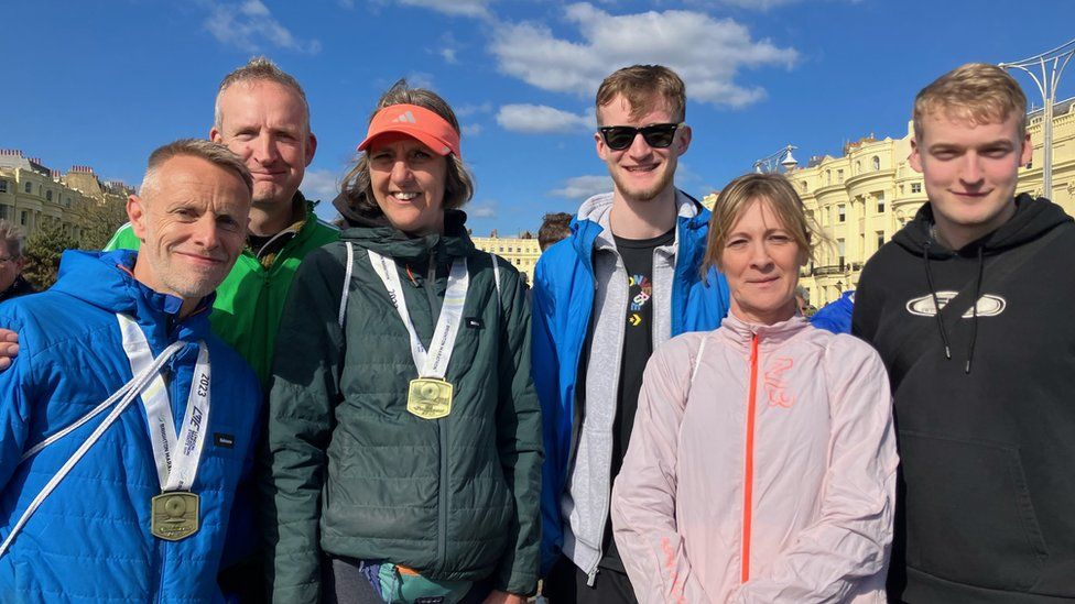 Mrs Blackwell and Ms Graimes posing for a photo with their medals after running the Brighton Marathon. They are standing with Ms Blackwell's husband and three other men.