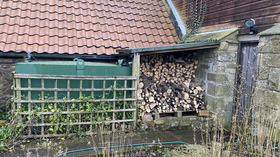 An image of a heating oil tank with a wood pile next to it