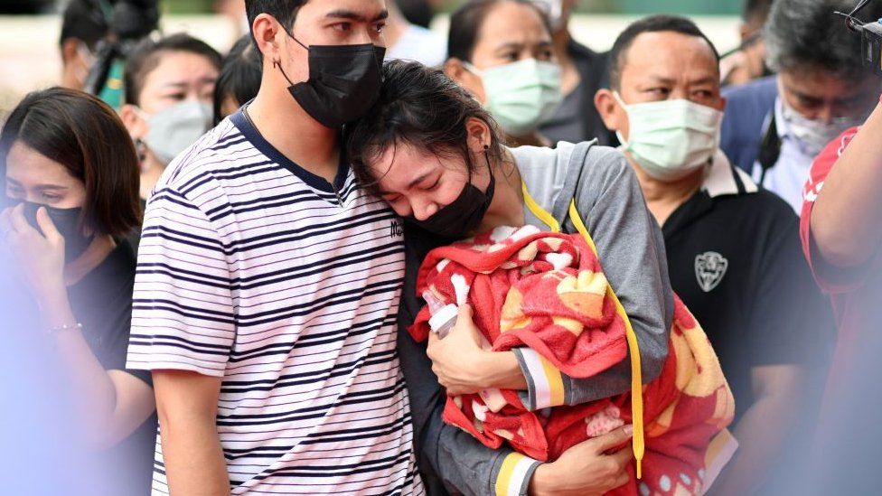 The mother of a victim holds a milk bottle and blanket as she reacts while standing outside the nursery in Na Klang in Thailand's northeastern Nong Bua Lam Phu province on October 7, 2022