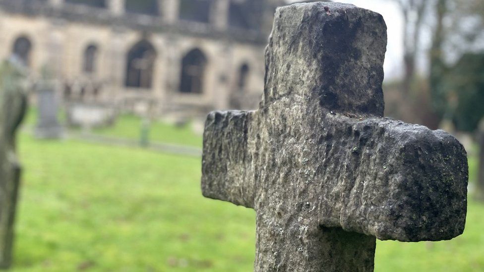 A stone cross against the blurred background of Malmesbury Abbey