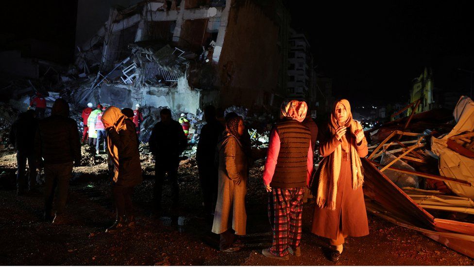 People look at a collapsed building near a bonfire, following an earthquake in Iskenderun, Turkey February 6, 2023