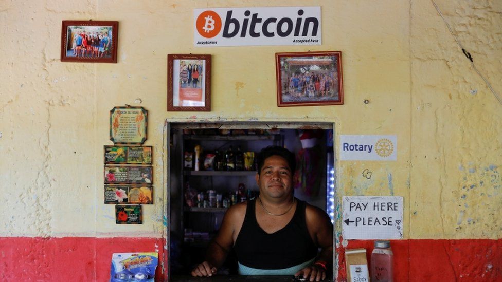 A man standing at his shop which accepts bitcoin as payment
