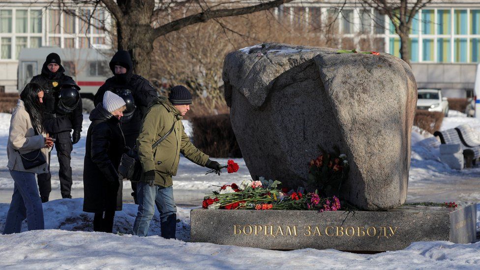 People laying floral tributes at a stone covered in snow