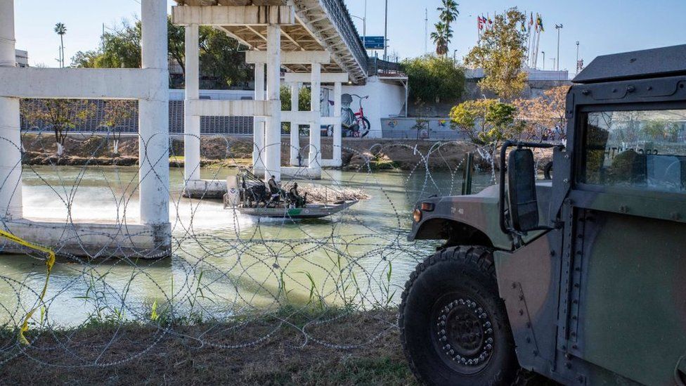 A Customs and Border Patrol boat in the Rio Grande near military vehicles in Eagle Pass in November 2021