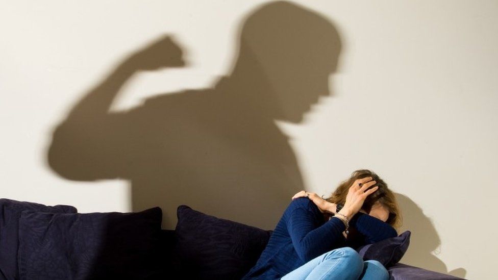 Woman cowering with man's shadow showing a clenched fist over her