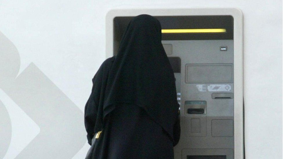 a woman in an abaya taking money out of a bank machine