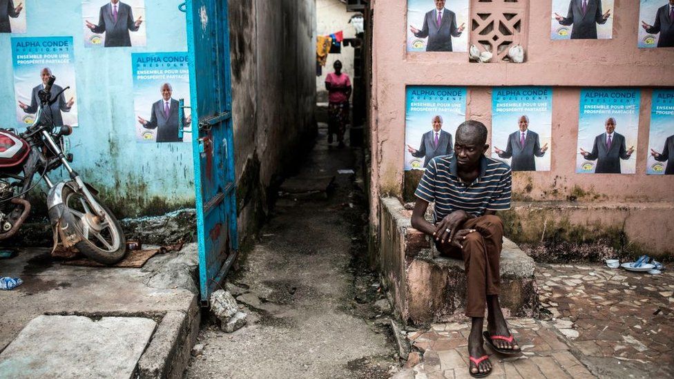A man sits in front of campaign posters of President Alpha Conde in Conakry, on October 13, 2020.