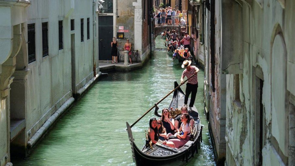 Gondoliers row their gondolas through the Venice Canal