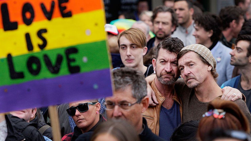 Two men embrace behind a sign saying "love is love" at a rally for marriage equality in Australia