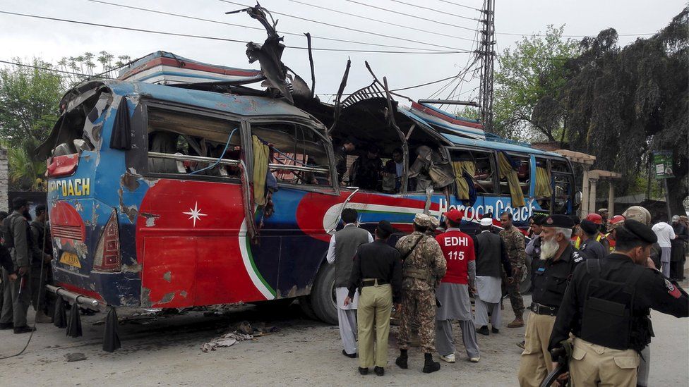 Policemen and rescue officials walk near a bus damaged in a bomb blast in Peshawar
