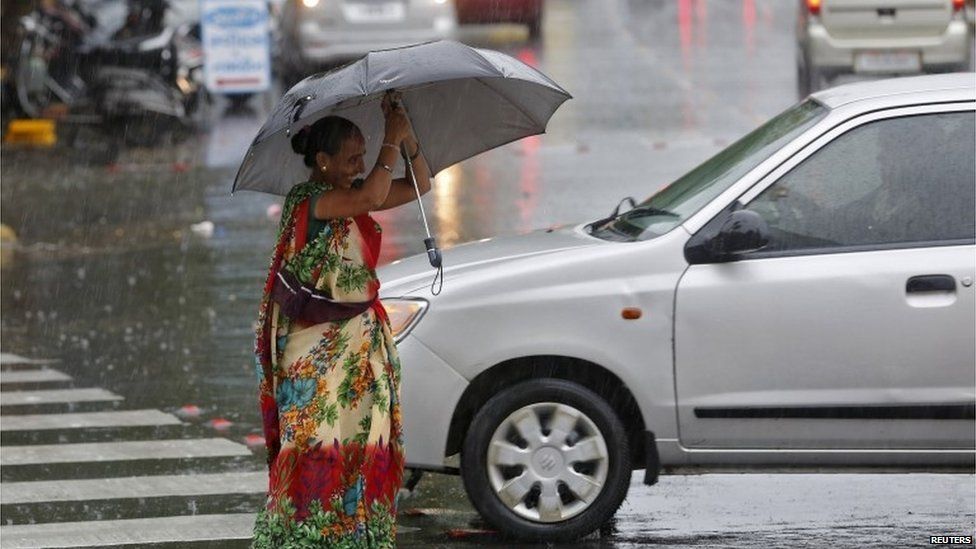 A woman tries to hold an umbrella as she walks through a busy road during a rain shower in Ahmedabad, India, June 24, 2015.
