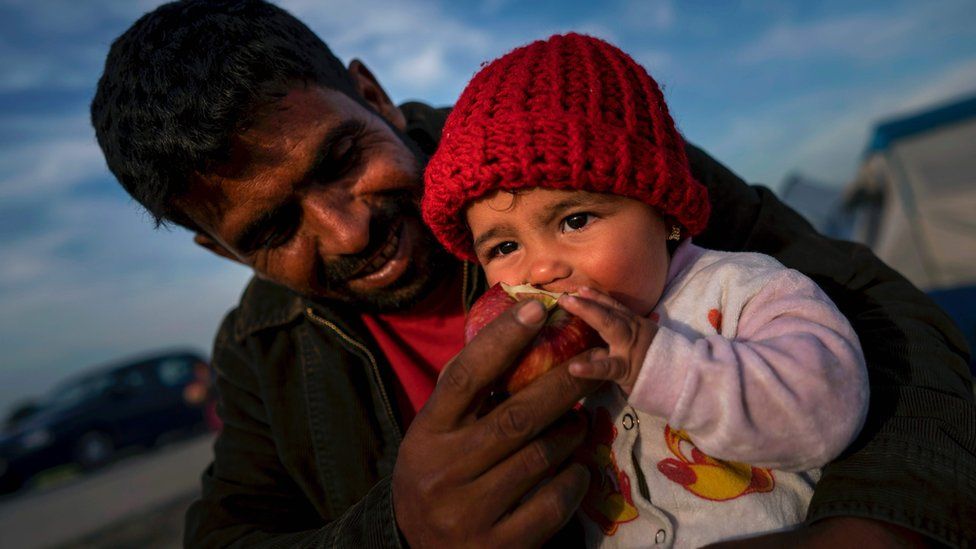 A refugee feeds his baby with an apple at sunset at a makeshift camp for migrants and refugees at the Greek-Macedonian border near the village of Idomeni on 27 April 2016