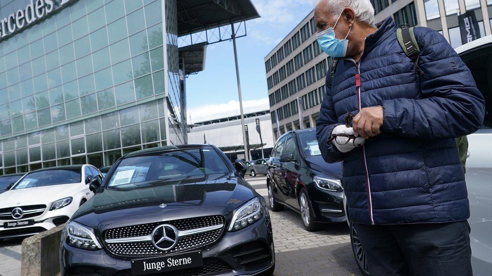 A man wearing a surgical mask stands at a Mercedes-Benz dealership where he said he is considering buying a car during the coronavirus crisis on May 05, 2020 in Berlin, Germany.