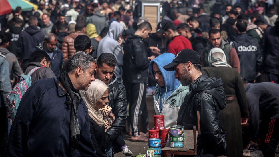 Palestinians sell cans of food in Rafah as they are surrounded by hundreds of other people
