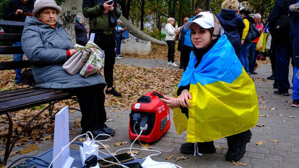 Woman draped in Ukrainian flag uses generator to charge phone