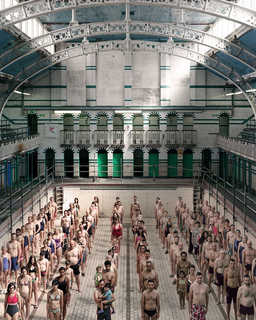 Dozens of swimmers stand on the bottom of an empty indoor swimming pool