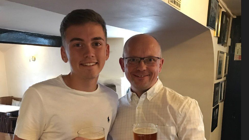 Two men, one younger than the other, both wearing white shirts and holding pints of beer