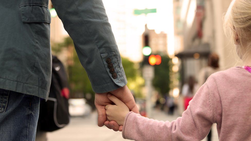 A close up of a father holding his daughter's hand as they walk along the street