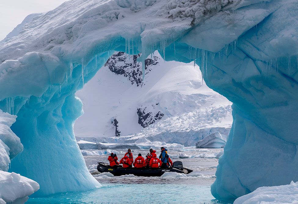 Туристы исследуют арку айсберга в бухте Сьерва вдоль западного побережья Земли Грэма, Антарктический полуостров, Антарктида
