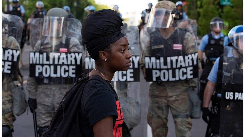 A demonstrator walks in front of a row of military police outside the White House
