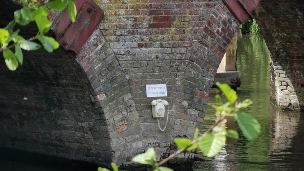 A white phone with an "Emergency Flood Line" sign above it on the buttress of Sonning Bridge