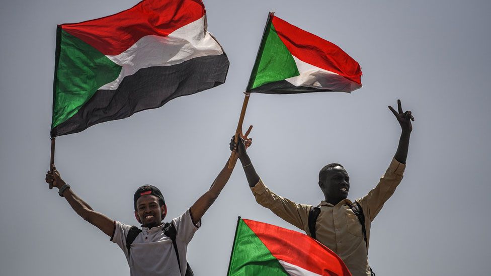 Sudanese protesters flash the victory sign and wave national flags during a rally outside the army headquarters in the capital Khartoum on April 19, 2019.