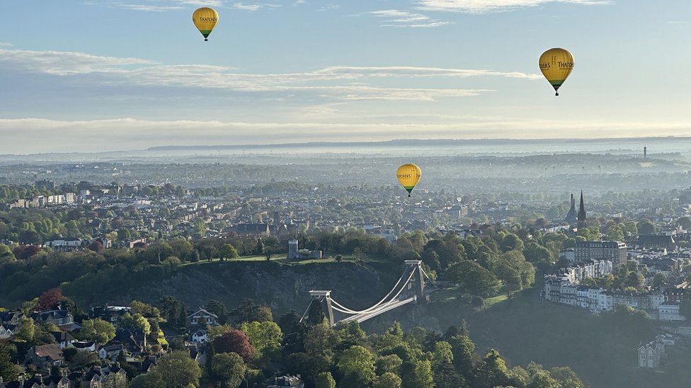 Three hot air balloons over Bristol with the Clifton Suspension Bridge in the foreground on a sunny day