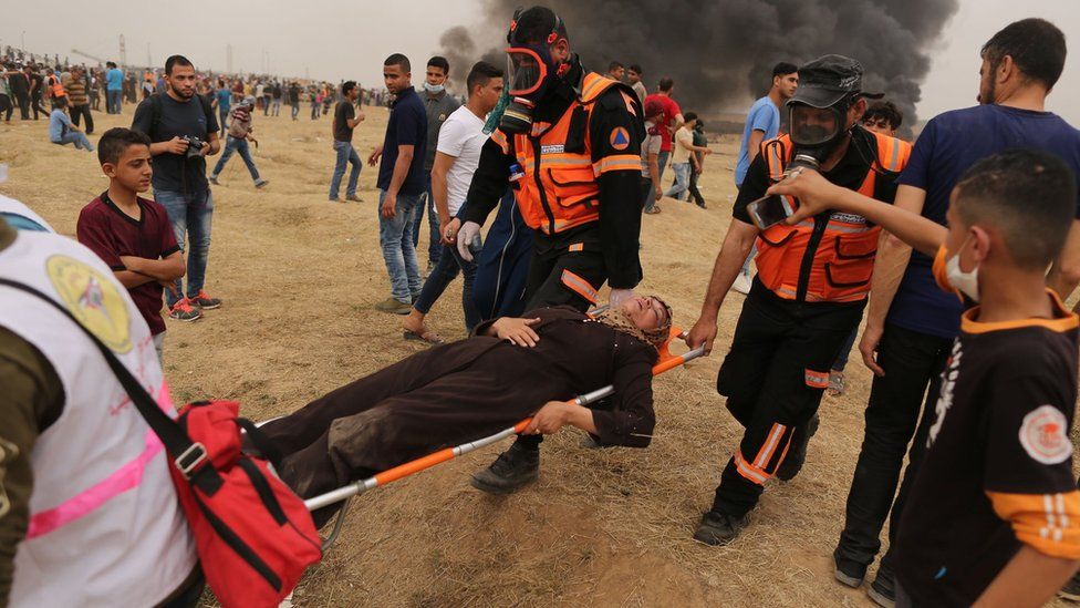 Palestinian medics carry an injured Palestinian woman during a protest near the Gaza-Israel border fence on 4 May 2018