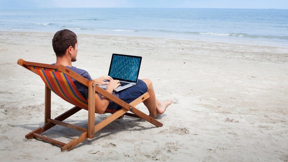 Man on laptop while sitting in a deckchair on a beach