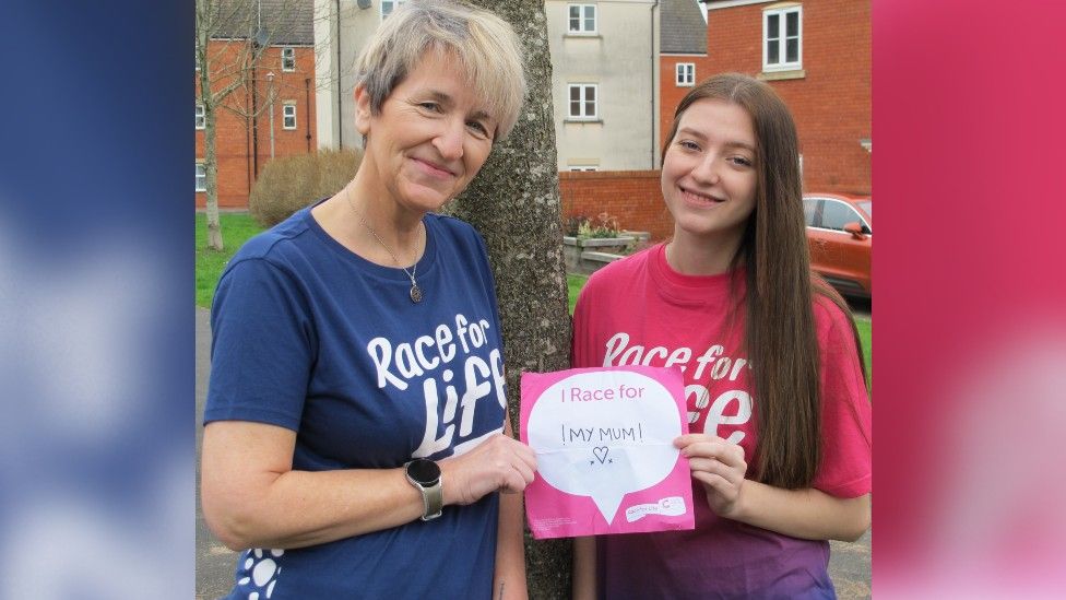 Jacqui and Jaigh in their Race For Life t shirts, holding a sign that says "I race for my mum"