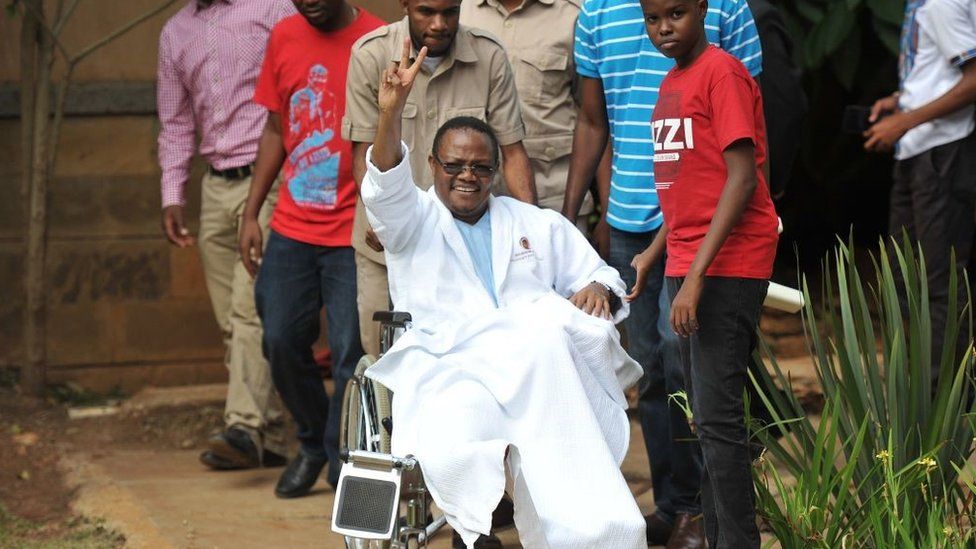 Tanzania Opposition lawmaker Tundu Lissu waves from his wheelchair after giving a press conference surrounded by members of his family and supporters on January 5, 2018 at a hospital in the Kenyan capital, Nairob