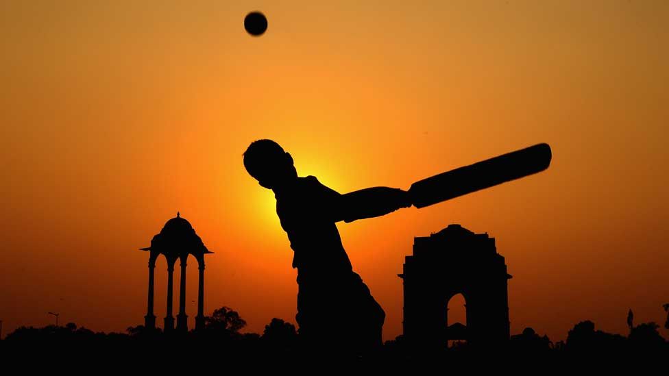 Silhouetted boy bats a ball away against the light of an Indian sunset