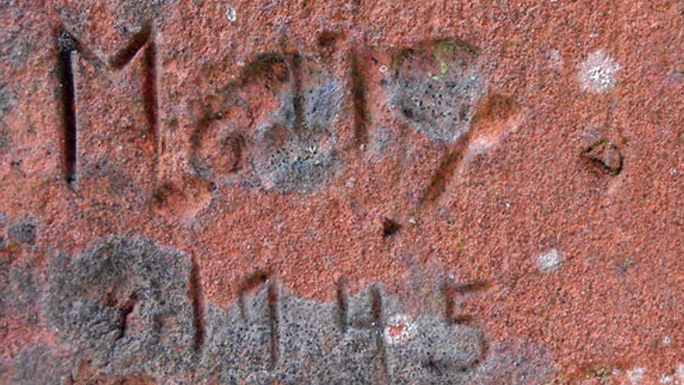 A close-up of 'Mary, 1945' carved into red brick