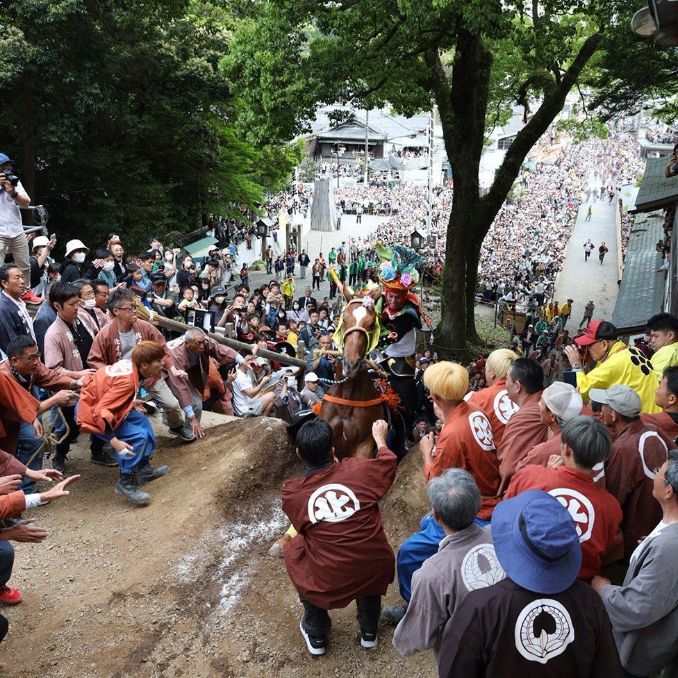 A horse and rider climb a steep earth wall surrounded by crowds at this year's Ageuma Shinji or Rising Horse Festival