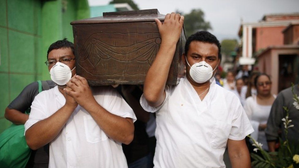 Men with their mouths covered wih surgical masks carry the coffin of a victim of the Cambray neighborhood mudslide, to the Santa Catarina Pinula cemetery on the outskirts of Guatemala City, Sunday, Oct. 4, 2015.