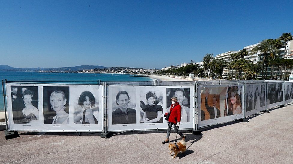 A woman walks past photos of the Cannes Film Festival on the Croisette in Cannes as a lockdown is imposed to slow the rate of the coronavirus in France, March 18, 2020.