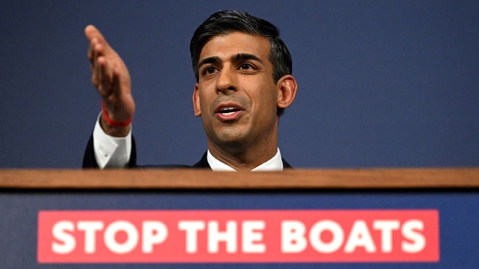 Rishi Sunak at a lectern with the slogan Stop the Boats