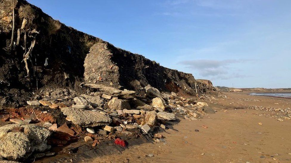 Debris including pipes and cables can be seen in the eroded cliffs